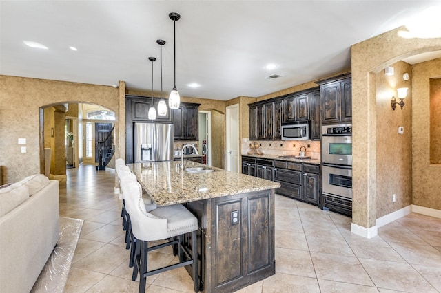 kitchen featuring appliances with stainless steel finishes, decorative light fixtures, sink, dark brown cabinetry, and a center island with sink