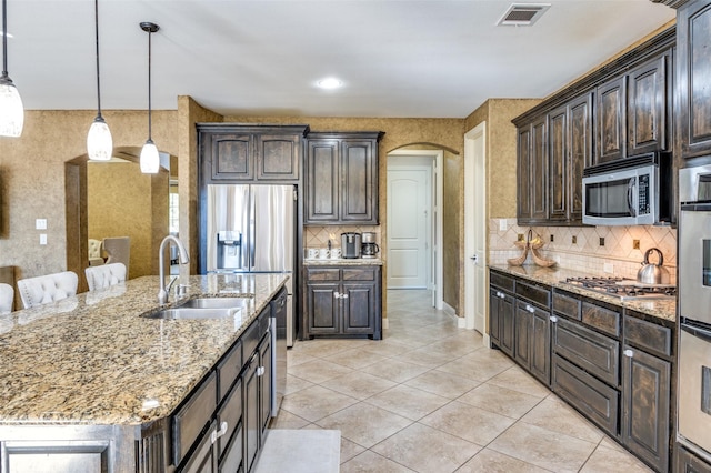 kitchen featuring dark brown cabinetry, sink, appliances with stainless steel finishes, light stone countertops, and a kitchen island with sink