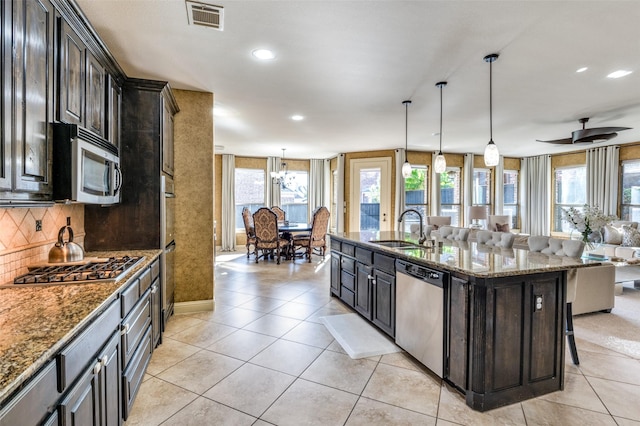 kitchen with a breakfast bar area, appliances with stainless steel finishes, dark stone countertops, an island with sink, and decorative light fixtures