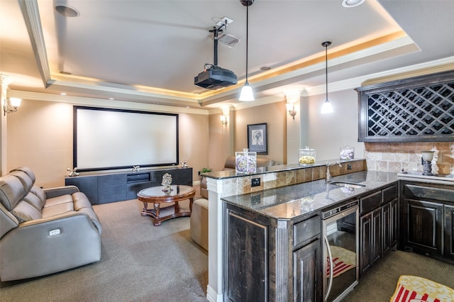 home theater featuring dark colored carpet, ornate columns, indoor wet bar, a tray ceiling, and beverage cooler