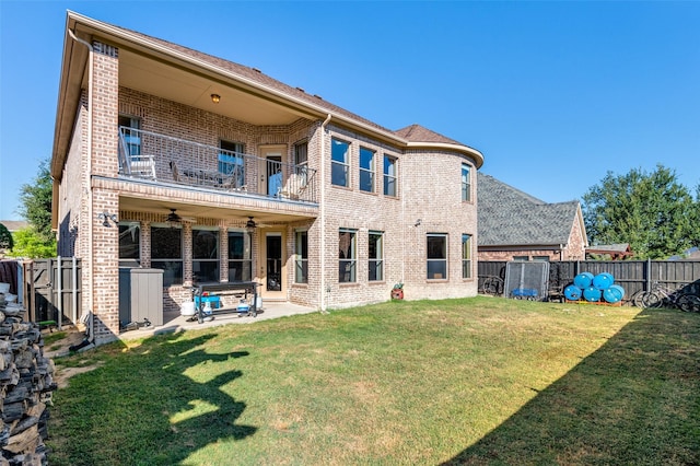 rear view of house with ceiling fan, a yard, a patio, and a balcony