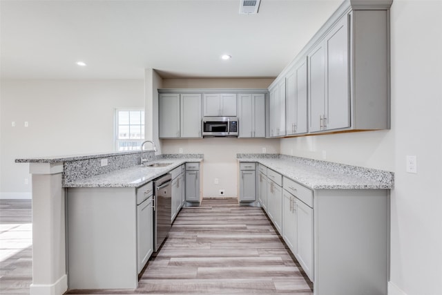 kitchen featuring sink, light stone counters, gray cabinets, stainless steel appliances, and light hardwood / wood-style floors