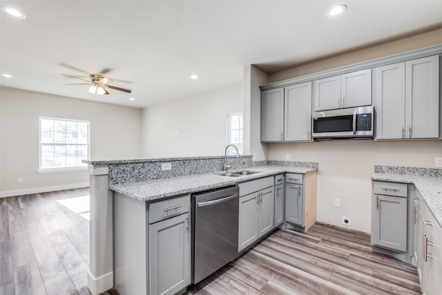 kitchen featuring sink, appliances with stainless steel finishes, gray cabinetry, light stone counters, and light hardwood / wood-style floors