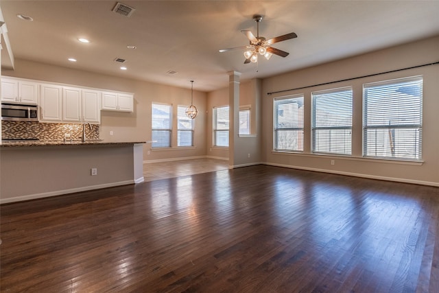 unfurnished living room with ornate columns, sink, ceiling fan with notable chandelier, and dark hardwood / wood-style flooring