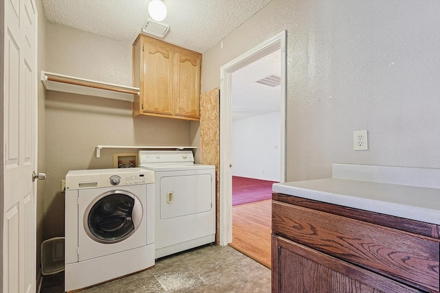 laundry room featuring separate washer and dryer, cabinets, and a textured ceiling