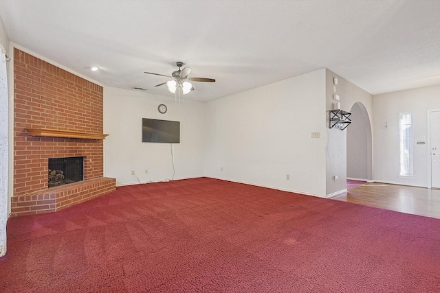 unfurnished living room featuring ceiling fan, carpet flooring, and a brick fireplace