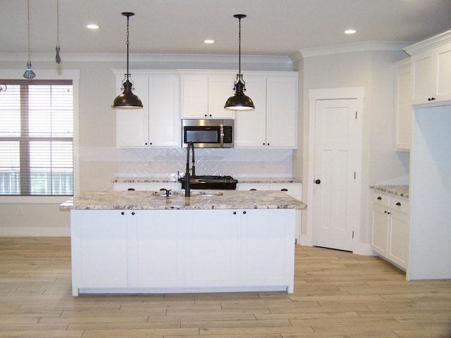 kitchen with white cabinetry, an island with sink, pendant lighting, and light stone counters