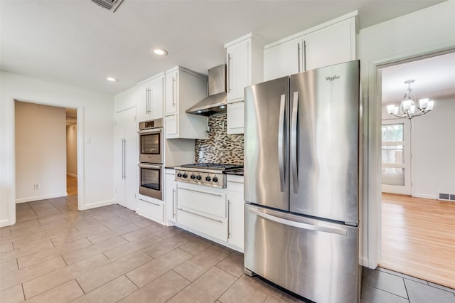 kitchen with stainless steel appliances, pendant lighting, wall chimney range hood, and white cabinets