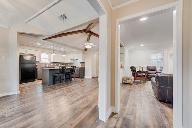 living room with ceiling fan, vaulted ceiling with beams, crown molding, and light wood-type flooring