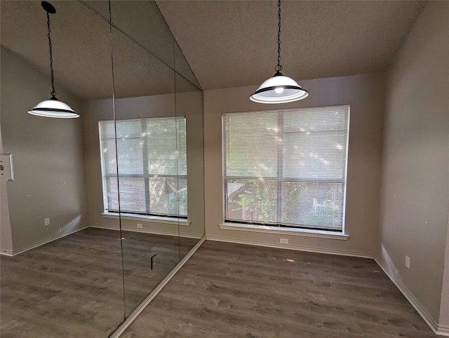 unfurnished dining area featuring dark hardwood / wood-style floors, vaulted ceiling, and a textured ceiling