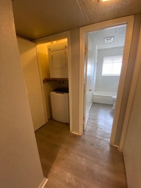 hallway with light hardwood / wood-style flooring, stacked washer and clothes dryer, and a textured ceiling