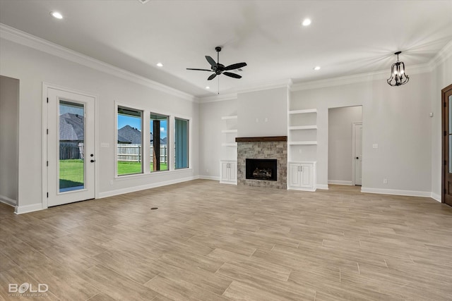 unfurnished living room with crown molding, ceiling fan with notable chandelier, built in shelves, a stone fireplace, and light wood-type flooring