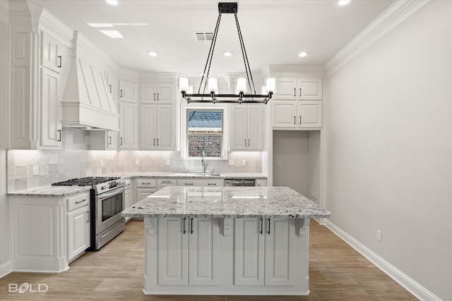 kitchen featuring stainless steel gas range, sink, white cabinetry, a kitchen island, and pendant lighting