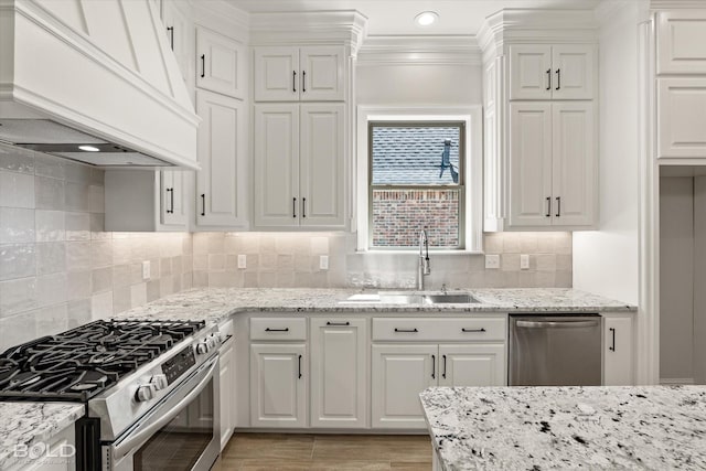 kitchen with sink, premium range hood, stainless steel appliances, light stone counters, and white cabinets