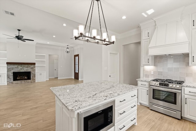 kitchen featuring stainless steel gas range, white cabinetry, black microwave, a kitchen island, and custom range hood