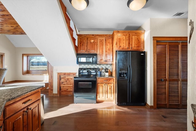 kitchen featuring lofted ceiling, dark stone countertops, backsplash, black appliances, and dark hardwood / wood-style flooring