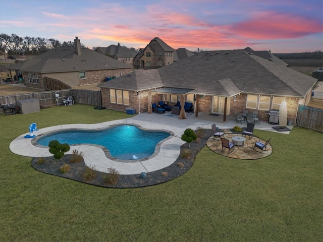 pool at dusk featuring a patio, an outdoor fire pit, and a lawn