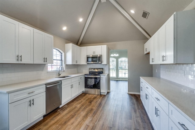 kitchen with white cabinetry, stainless steel appliances, sink, and vaulted ceiling with beams