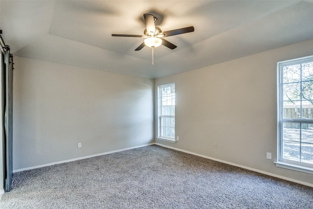 empty room with a tray ceiling, plenty of natural light, a barn door, and ceiling fan