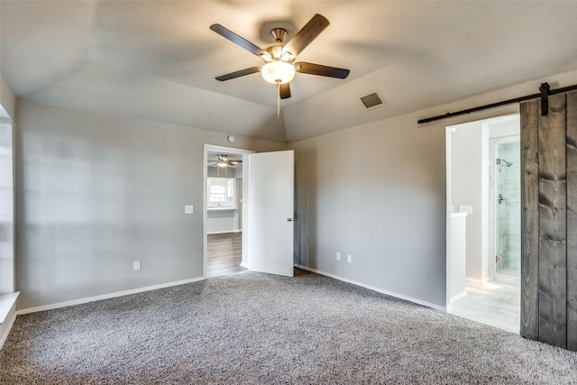 unfurnished bedroom featuring vaulted ceiling, connected bathroom, ceiling fan, a barn door, and light carpet