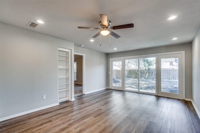 unfurnished room featuring dark wood-type flooring, ceiling fan, built in features, and a textured ceiling