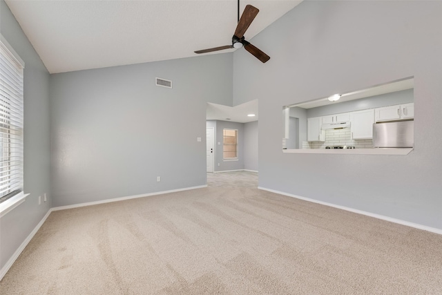 unfurnished living room featuring ceiling fan, a healthy amount of sunlight, high vaulted ceiling, and light carpet