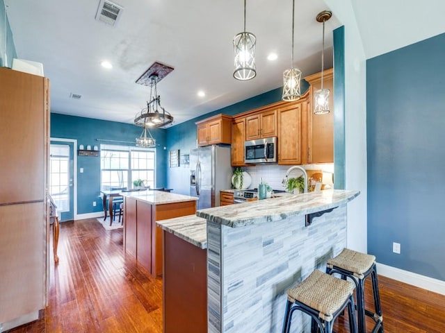 kitchen featuring light stone counters, decorative light fixtures, kitchen peninsula, a kitchen island, and stainless steel appliances