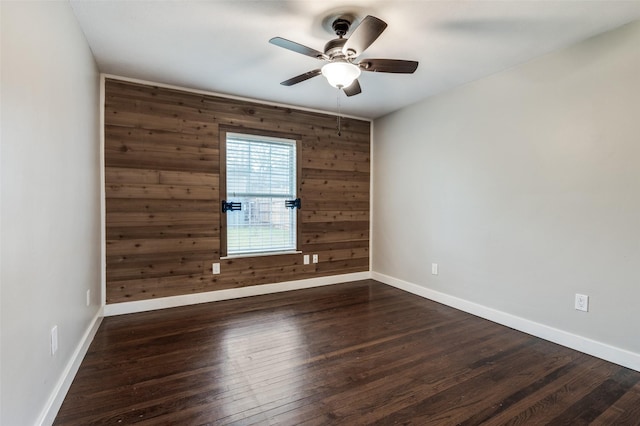 spare room featuring ceiling fan, dark hardwood / wood-style floors, and wooden walls