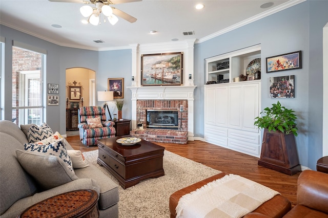 living room featuring a fireplace, wood-type flooring, ornamental molding, ceiling fan, and built in shelves