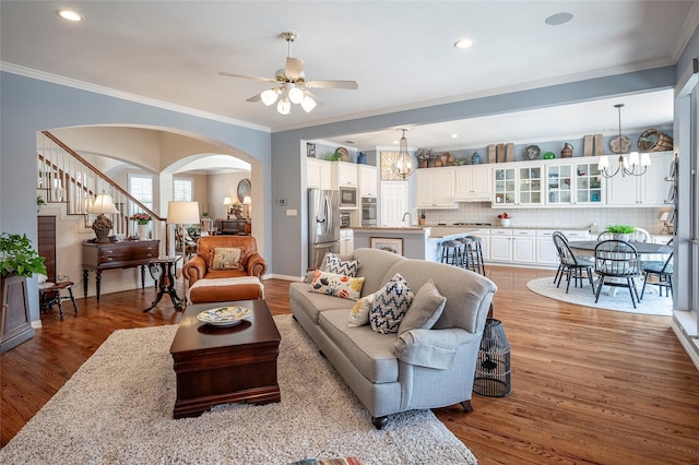 living room featuring crown molding, ceiling fan with notable chandelier, and light hardwood / wood-style floors