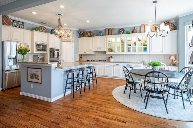 kitchen featuring pendant lighting, white cabinetry, a notable chandelier, stainless steel appliances, and a center island with sink