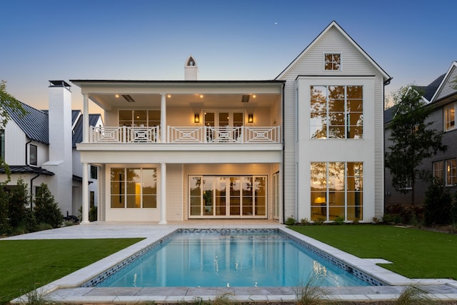 back house at dusk with a patio, a balcony, and a yard