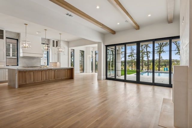 unfurnished living room featuring beamed ceiling, light hardwood / wood-style floors, and a chandelier