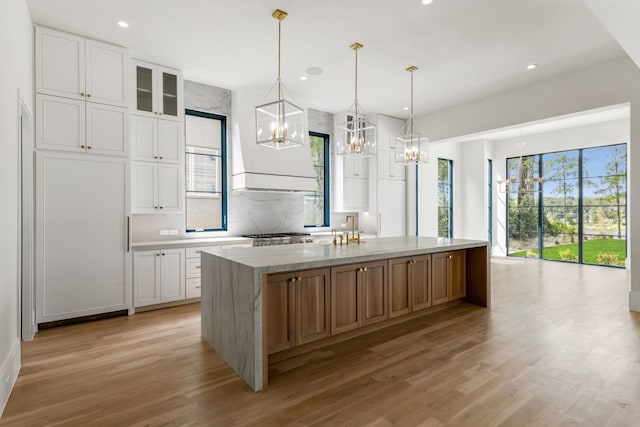 kitchen with white cabinetry, light stone counters, pendant lighting, and an island with sink