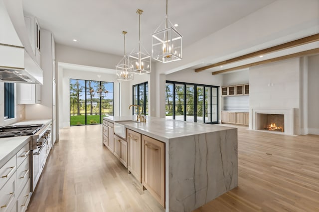 kitchen with decorative light fixtures, sink, a large fireplace, a large island, and light hardwood / wood-style flooring