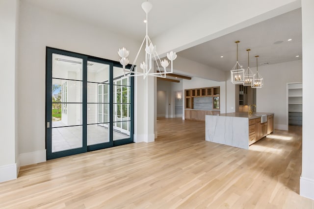 kitchen with light brown cabinetry, hanging light fixtures, a notable chandelier, kitchen peninsula, and light wood-type flooring