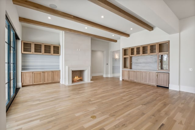 unfurnished living room with a large fireplace, beam ceiling, and light hardwood / wood-style flooring