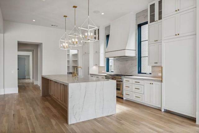 kitchen featuring white cabinetry, stainless steel range, light stone countertops, custom range hood, and light hardwood / wood-style flooring