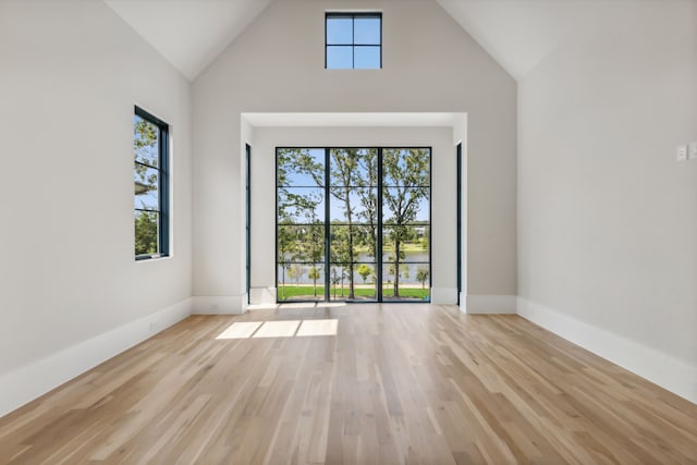 spare room with high vaulted ceiling and light wood-type flooring