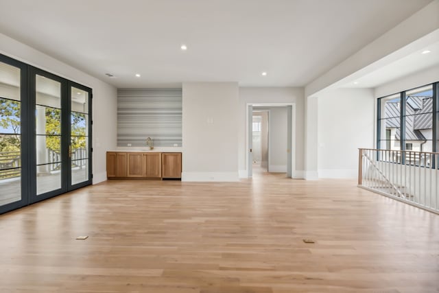 unfurnished living room featuring french doors, sink, and light hardwood / wood-style flooring