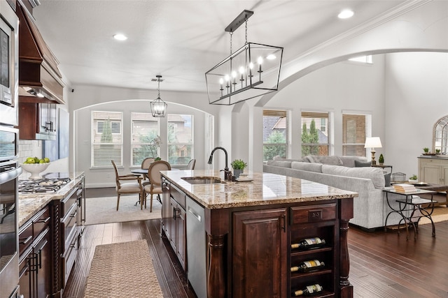 kitchen featuring sink, hanging light fixtures, stainless steel dishwasher, light stone countertops, and a kitchen island with sink