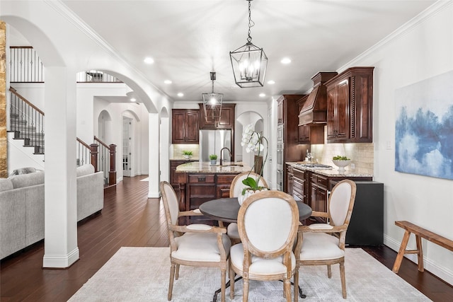 dining room featuring sink, dark wood-type flooring, ornamental molding, and a chandelier