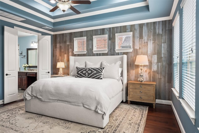 bedroom featuring connected bathroom, wood-type flooring, ornamental molding, a raised ceiling, and ceiling fan