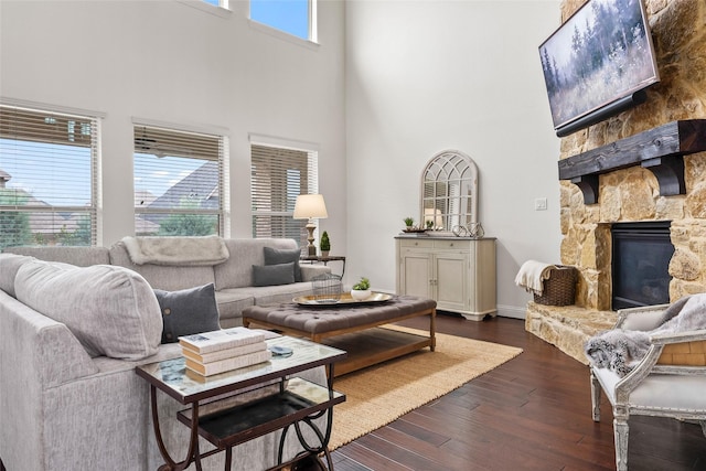 living room with a high ceiling, a stone fireplace, and dark wood-type flooring