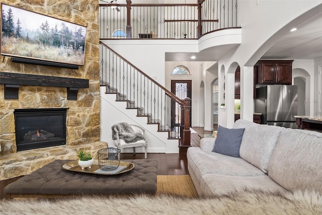 living room featuring a stone fireplace, dark wood-type flooring, and a towering ceiling