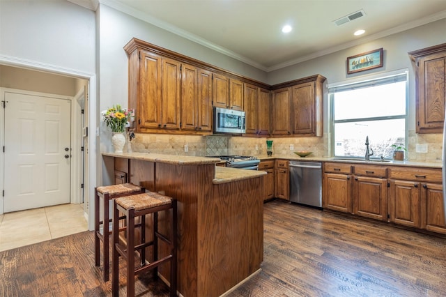 kitchen with sink, a kitchen bar, ornamental molding, kitchen peninsula, and stainless steel appliances