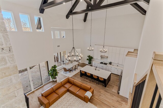 living room featuring beam ceiling, light wood-type flooring, high vaulted ceiling, and a notable chandelier