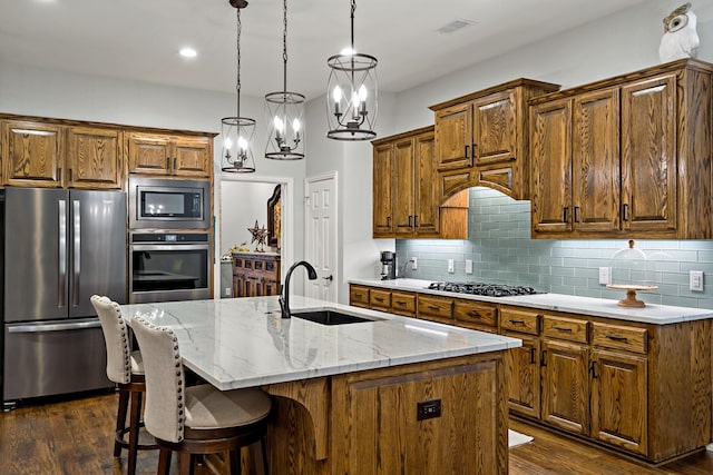 kitchen with pendant lighting, sink, stainless steel appliances, tasteful backsplash, and a center island with sink