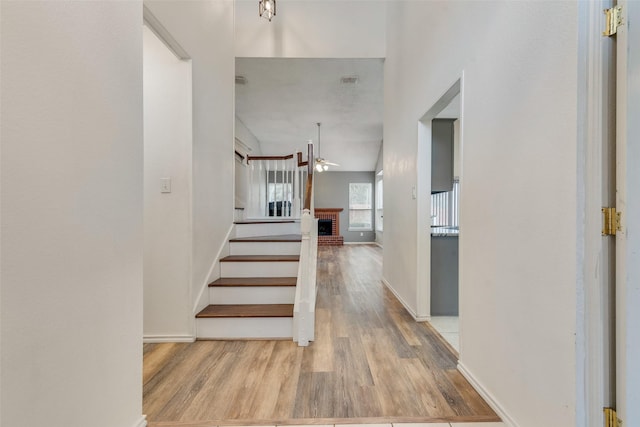 staircase with wood-type flooring, a brick fireplace, and ceiling fan