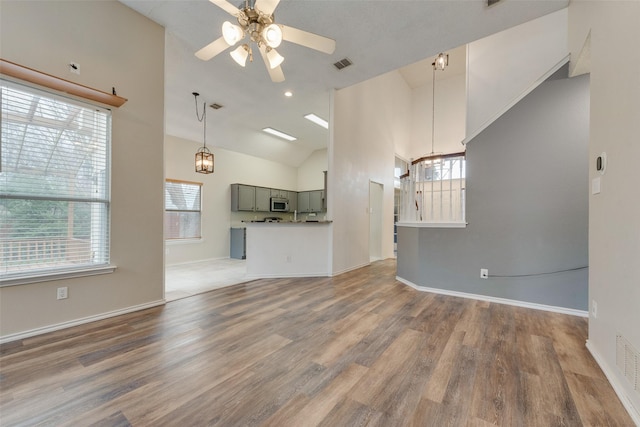 unfurnished living room with ceiling fan with notable chandelier, high vaulted ceiling, plenty of natural light, and hardwood / wood-style floors